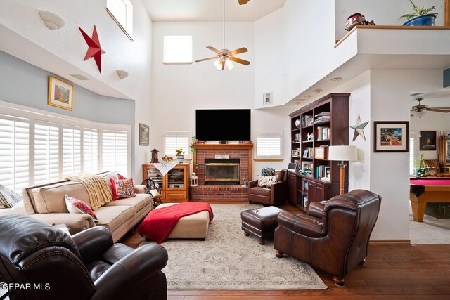 living room with ceiling fan, a fireplace, a towering ceiling, and dark wood-type flooring