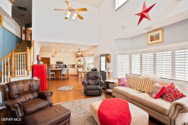 living area featuring a ceiling fan, stairs, visible vents, and wood finished floors