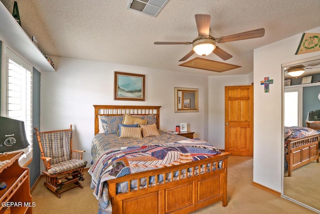 bedroom with light carpet, a textured ceiling, visible vents, and a ceiling fan