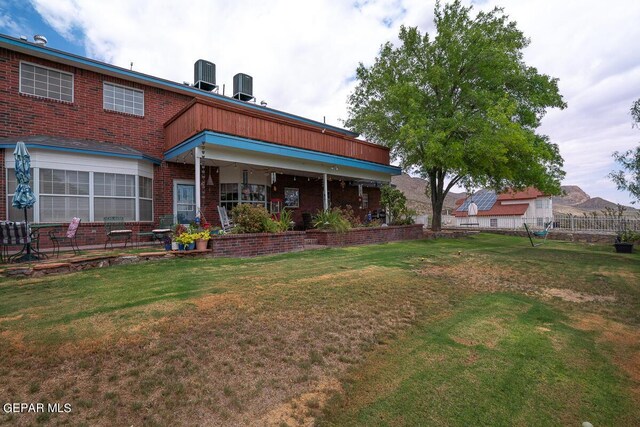 rear view of property featuring brick siding, a lawn, and cooling unit