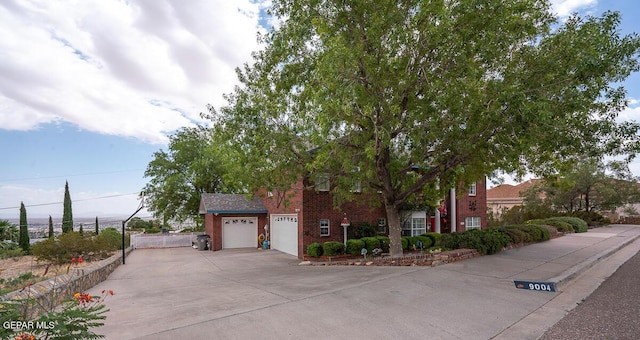 view of property hidden behind natural elements with brick siding, driveway, and fence