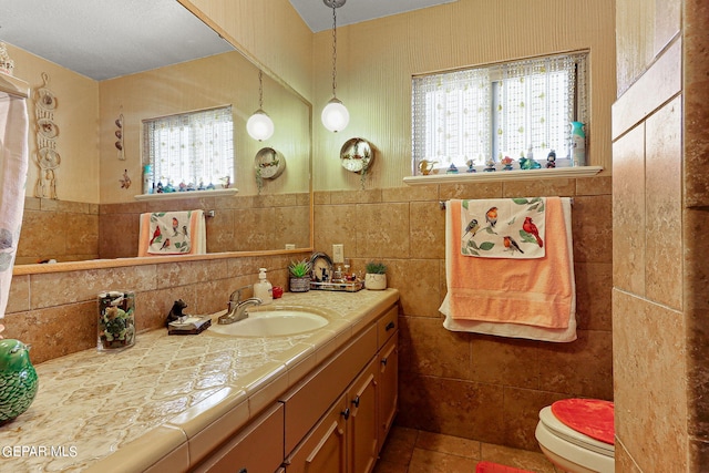 bathroom with wainscoting, toilet, tile patterned floors, vanity, and tile walls