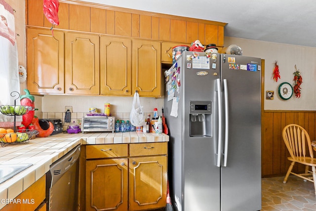 kitchen with stainless steel appliances, wainscoting, tile counters, and wooden walls