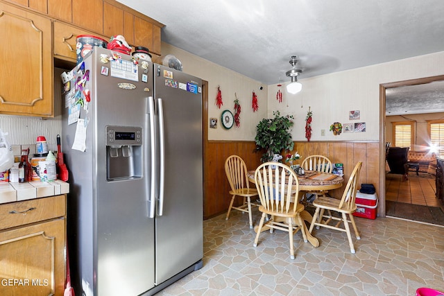 kitchen featuring wainscoting, tile countertops, stainless steel fridge with ice dispenser, stone finish floor, and a textured ceiling