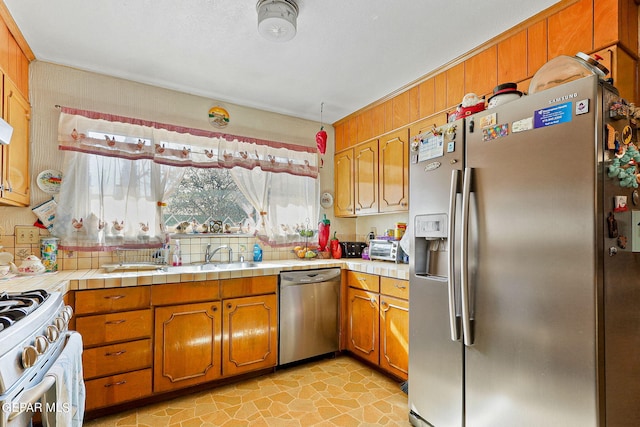 kitchen featuring stainless steel appliances, tile counters, brown cabinetry, and a sink