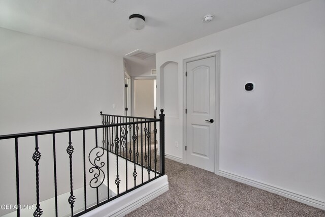 hallway featuring an upstairs landing, baseboards, visible vents, and light colored carpet