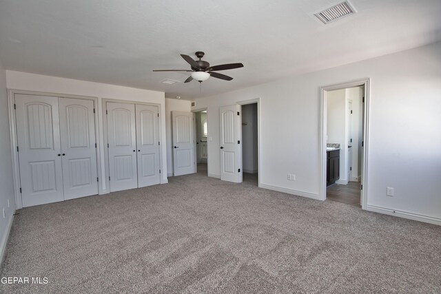 unfurnished bedroom featuring light carpet, baseboards, visible vents, ensuite bathroom, and multiple closets