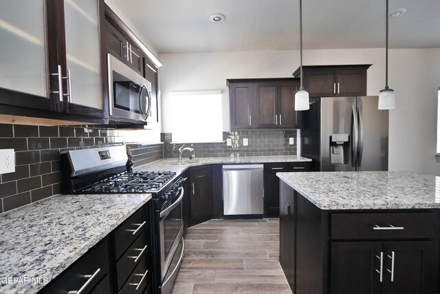 kitchen with wood finished floors, dark brown cabinets, appliances with stainless steel finishes, a center island, and decorative light fixtures