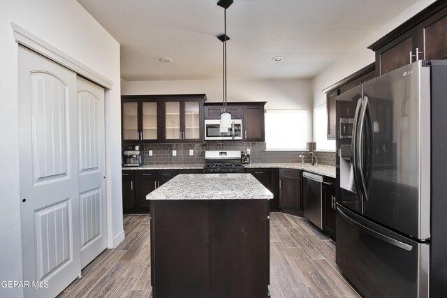 kitchen featuring pendant lighting, appliances with stainless steel finishes, glass insert cabinets, a kitchen island, and wood finished floors