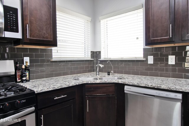 kitchen with tasteful backsplash, light stone counters, stainless steel appliances, and a sink