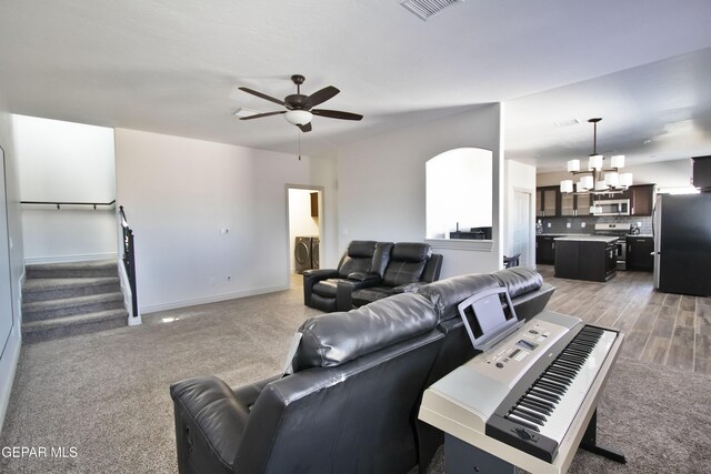 carpeted living area with visible vents, stairway, baseboards, and ceiling fan with notable chandelier