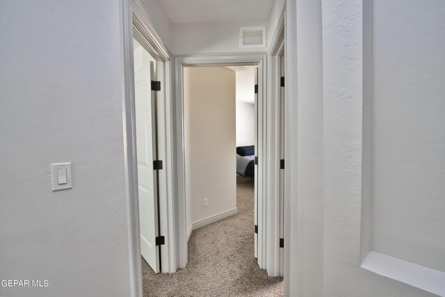 hallway featuring light carpet, visible vents, and a textured wall