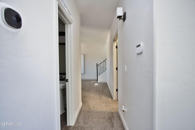 corridor with baseboards, stairway, and light colored carpet