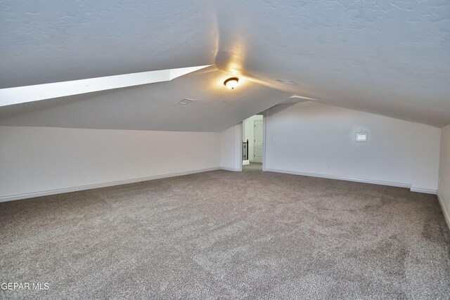 bonus room featuring lofted ceiling, a textured ceiling, carpet flooring, and baseboards