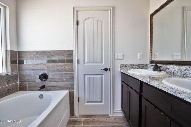 bathroom with a bath, double vanity, a sink, and wood finished floors