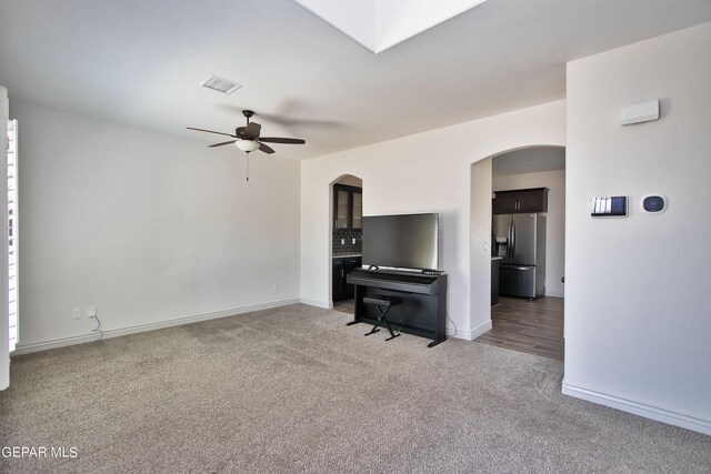 unfurnished living room with visible vents, arched walkways, baseboards, ceiling fan, and carpet floors