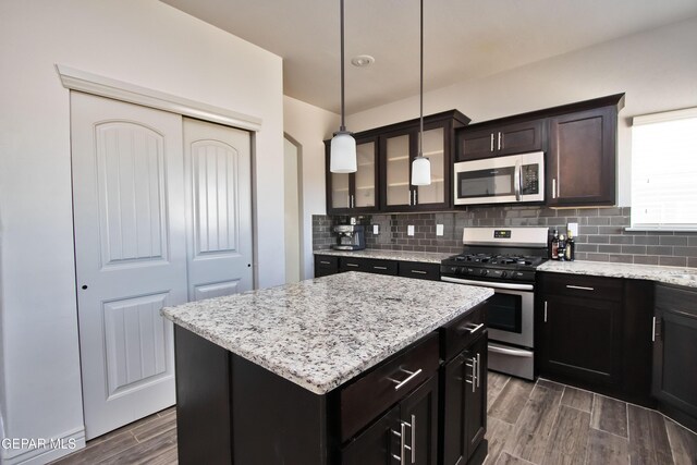 kitchen with a center island, wood finish floors, decorative light fixtures, appliances with stainless steel finishes, and glass insert cabinets