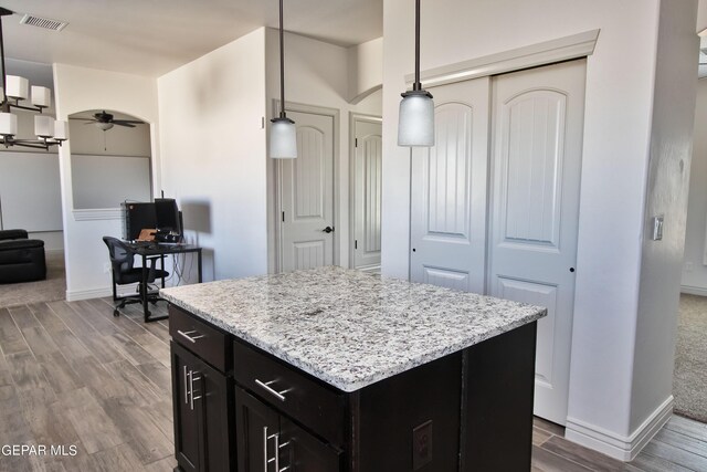 kitchen with wood finish floors, a kitchen island, visible vents, a ceiling fan, and hanging light fixtures