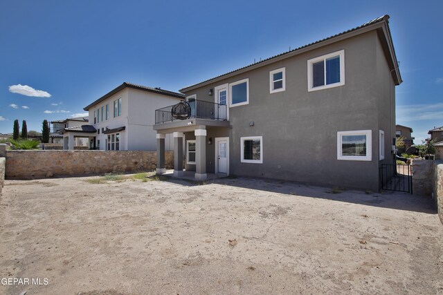 rear view of property with fence, a balcony, and stucco siding