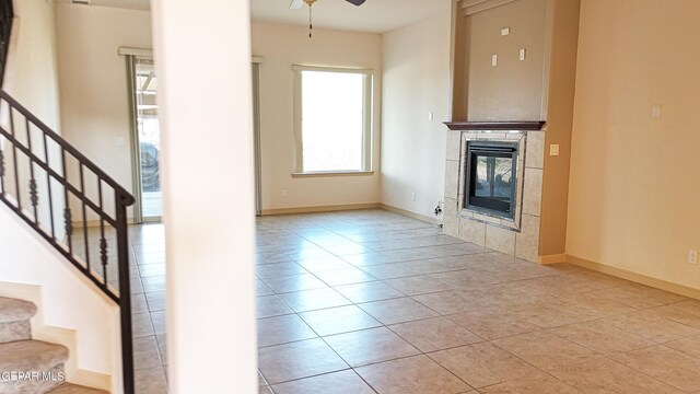 unfurnished living room with ceiling fan, light tile patterned floors, and a tiled fireplace