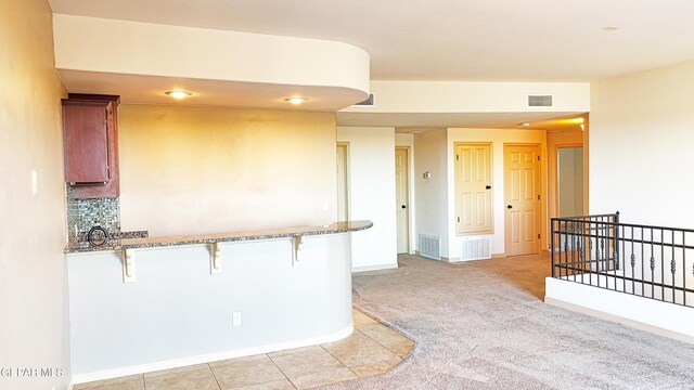 kitchen featuring a kitchen breakfast bar, light stone counters, light carpet, and tasteful backsplash