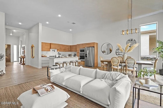 living room with a towering ceiling, sink, and light wood-type flooring