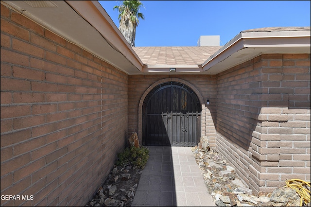 doorway to property featuring brick siding and a shingled roof