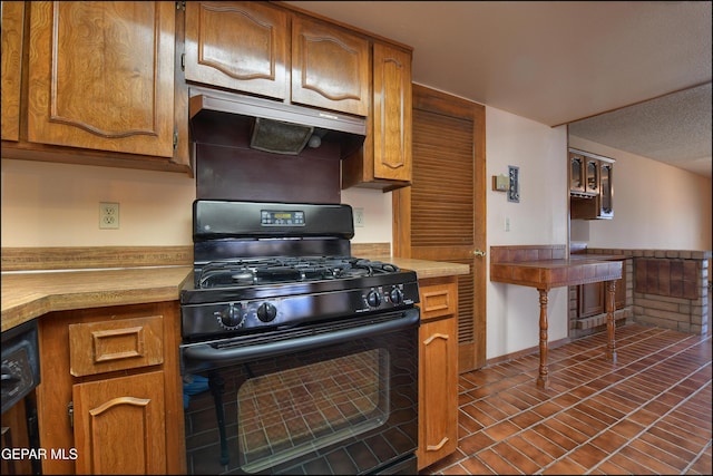 kitchen featuring brown cabinetry, under cabinet range hood, light countertops, and black gas range oven