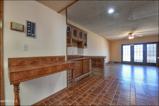 kitchen with glass insert cabinets, brown cabinetry, ceiling fan, a textured ceiling, and a peninsula