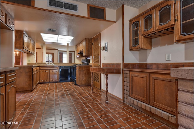 kitchen featuring visible vents, brown cabinetry, glass insert cabinets, a textured ceiling, and black appliances