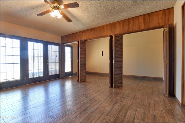 unfurnished room with a textured ceiling, ceiling fan, dark wood-type flooring, and baseboards