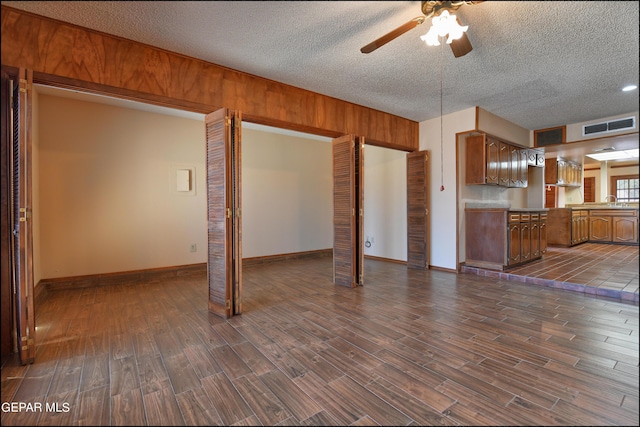 unfurnished living room featuring dark wood finished floors, visible vents, a ceiling fan, wood walls, and a textured ceiling