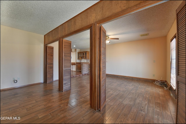 spare room featuring a textured ceiling, ceiling fan, visible vents, baseboards, and dark wood finished floors