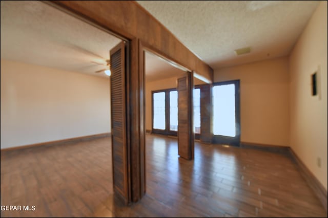 unfurnished room featuring a textured ceiling, dark wood-style flooring, a ceiling fan, and baseboards