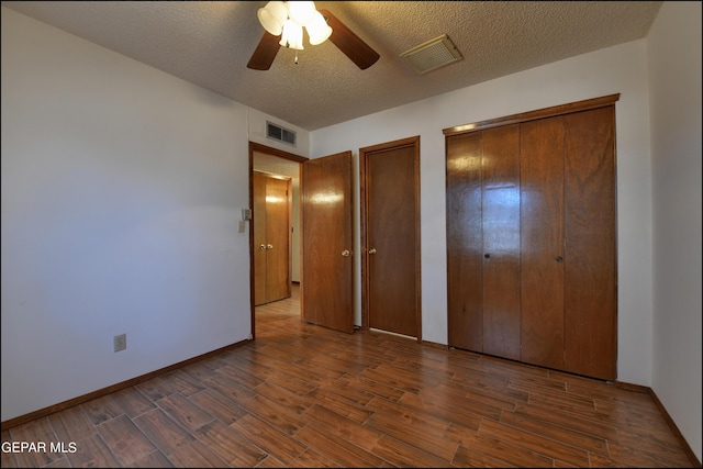 unfurnished bedroom with a textured ceiling, dark wood finished floors, visible vents, and multiple closets