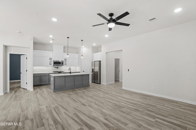 kitchen with appliances with stainless steel finishes, an island with sink, tasteful backsplash, ceiling fan, and white cabinetry