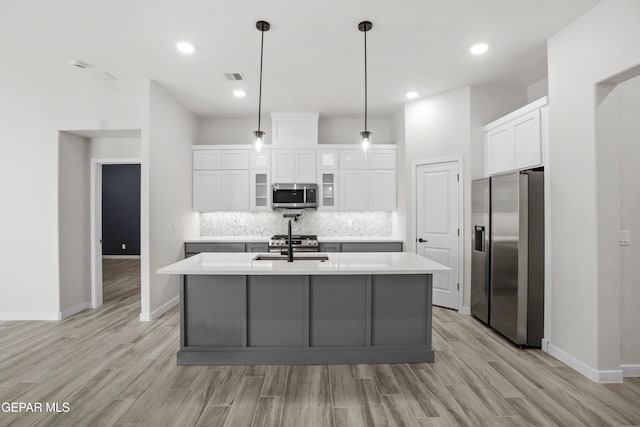 kitchen featuring decorative backsplash, light wood-type flooring, a kitchen island with sink, white cabinets, and appliances with stainless steel finishes