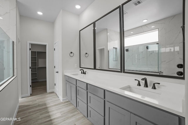 bathroom featuring a sink, visible vents, a marble finish shower, double vanity, and a walk in closet