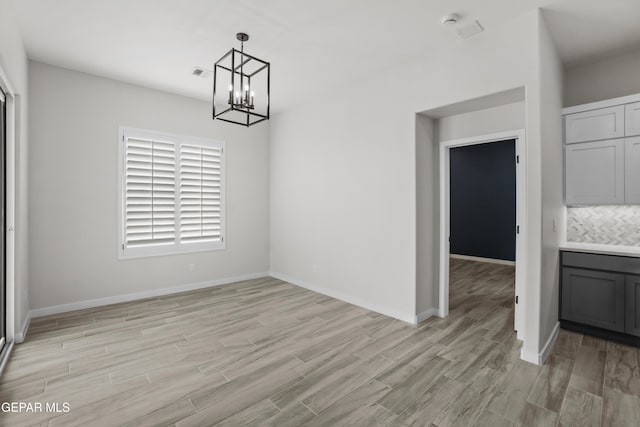 unfurnished dining area featuring a chandelier, light wood-type flooring, visible vents, and baseboards