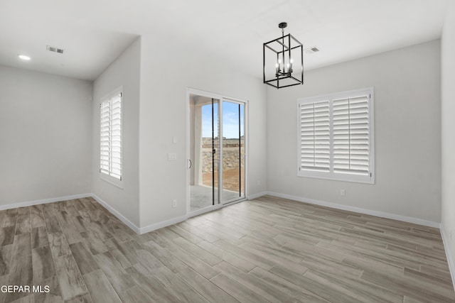 spare room featuring light wood finished floors, baseboards, visible vents, and an inviting chandelier