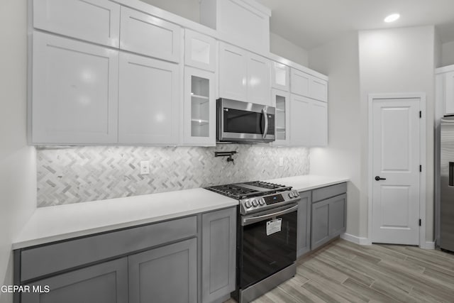 kitchen with appliances with stainless steel finishes, gray cabinets, light countertops, and glass insert cabinets