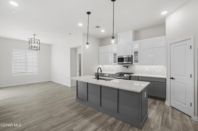 kitchen featuring an island with sink, glass insert cabinets, appliances with stainless steel finishes, light countertops, and a sink