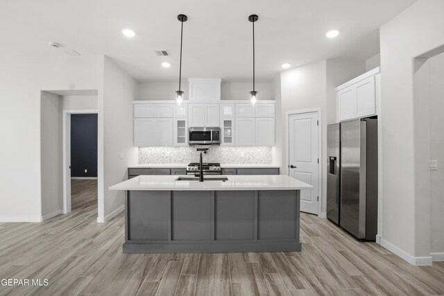 kitchen featuring appliances with stainless steel finishes, light countertops, a center island with sink, and white cabinetry