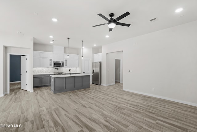 kitchen featuring decorative light fixtures, stainless steel appliances, light countertops, visible vents, and an island with sink