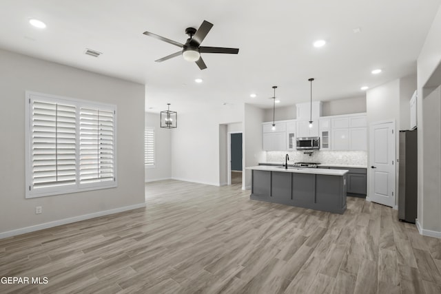 kitchen featuring pendant lighting, light countertops, appliances with stainless steel finishes, a kitchen island with sink, and white cabinetry