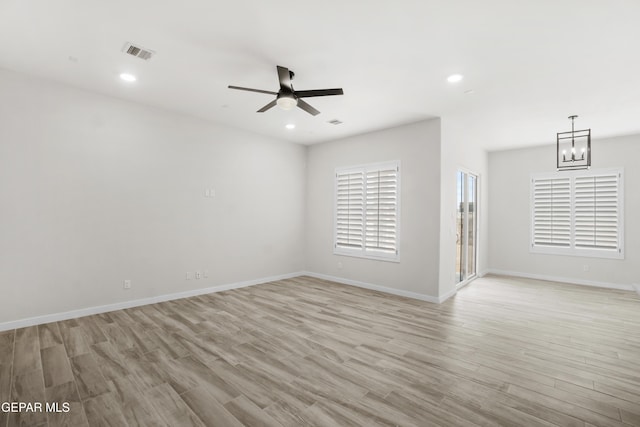 unfurnished room with ceiling fan with notable chandelier, light wood-type flooring, visible vents, and baseboards