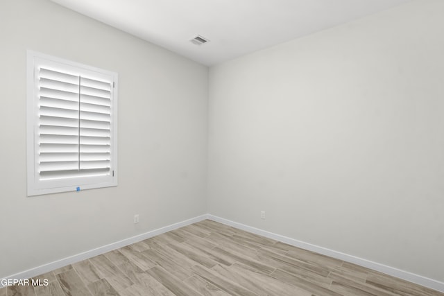 spare room featuring light wood finished floors, visible vents, and baseboards