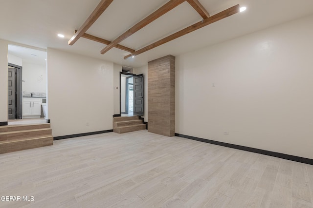 spare room featuring beamed ceiling, light wood-type flooring, and baseboards