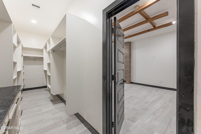 spacious closet with visible vents, beam ceiling, and light wood finished floors