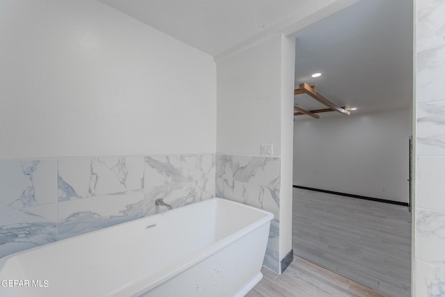 full bath featuring tile walls, a freestanding tub, and wood finished floors